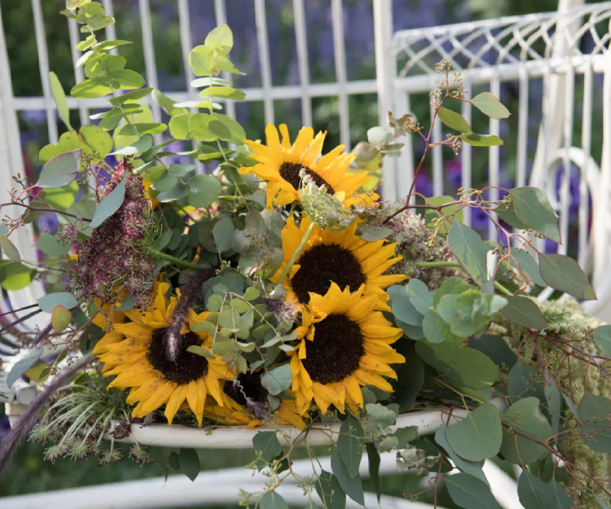 A bouquet of sunflowers and mixed greenery placed on a white outdoor chair.