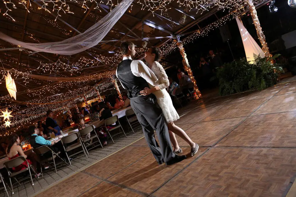 A couple dances closely at a dimly lit venue decorated with twinkling string lights and star ornaments, with seated guests in the background.