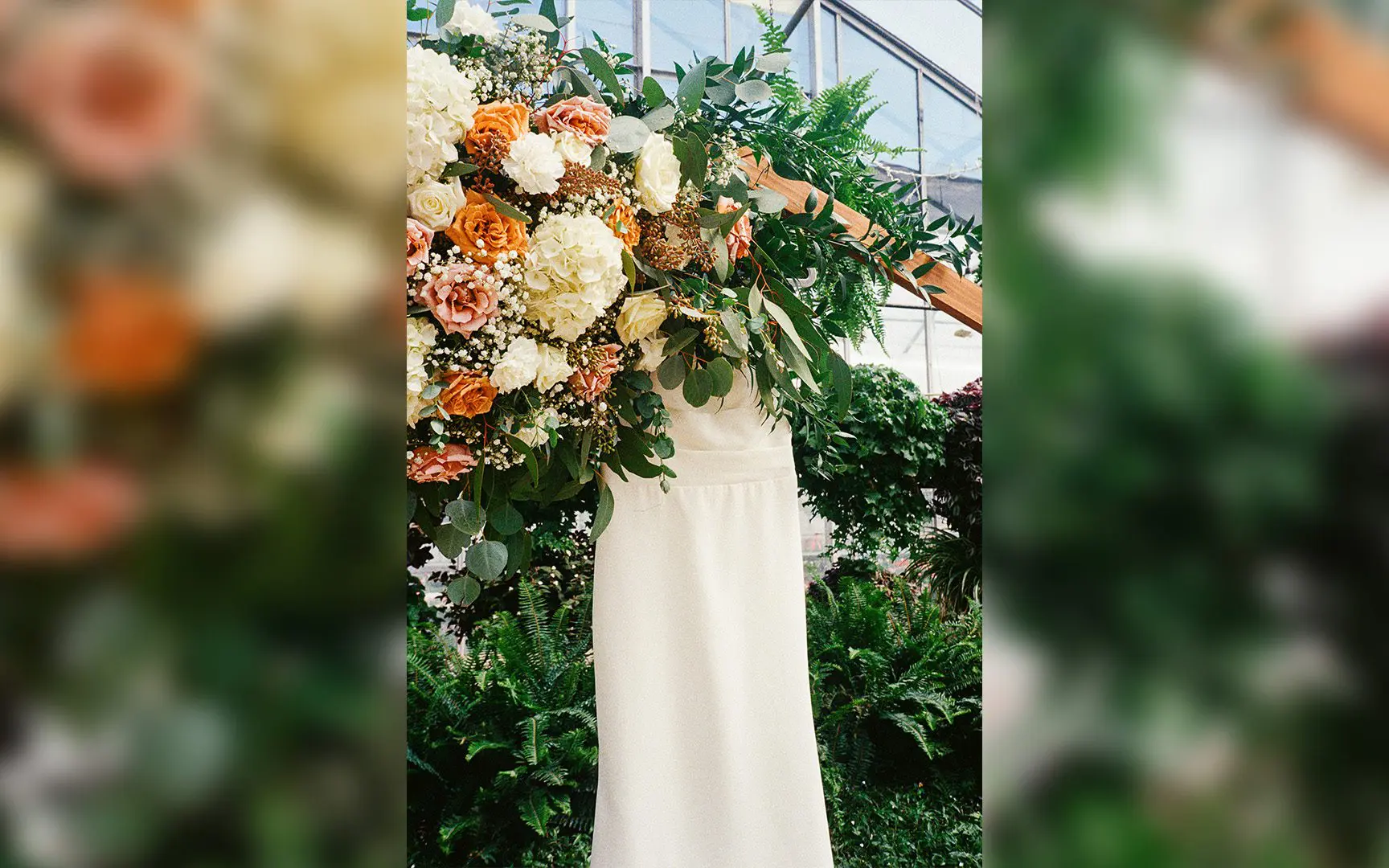 A wedding dress mannequin surrounded by vibrant floral arrangements in a greenhouse setting.
