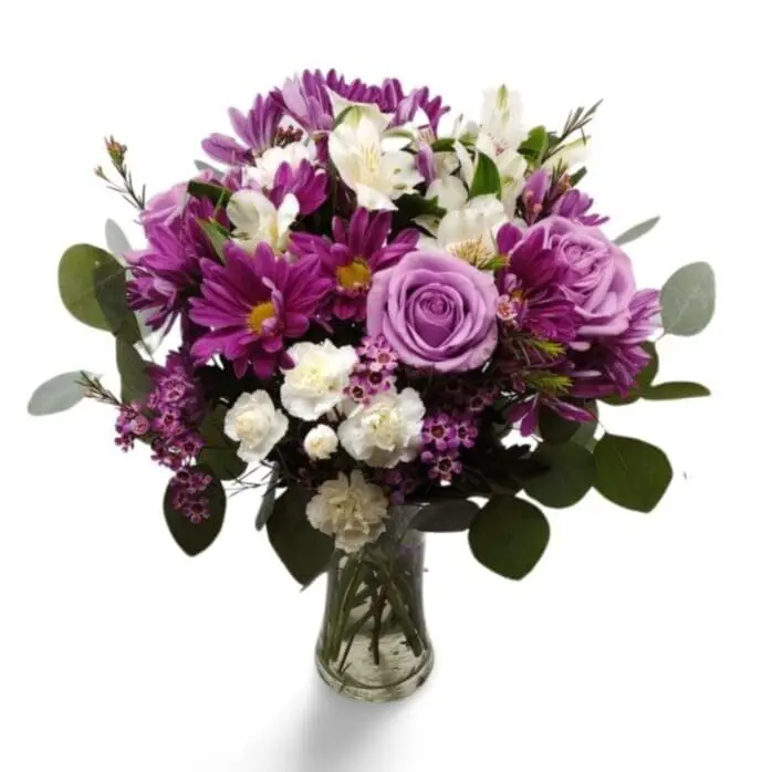 Perfectly pretty with lively purple roses, cheerful purple daisies, and a touch of white Peruvian lilies and mini carnations, this vibrant arrangement is sprinkled with touches of purple waxflower and lush greenery, all presented in a clear glass vase.