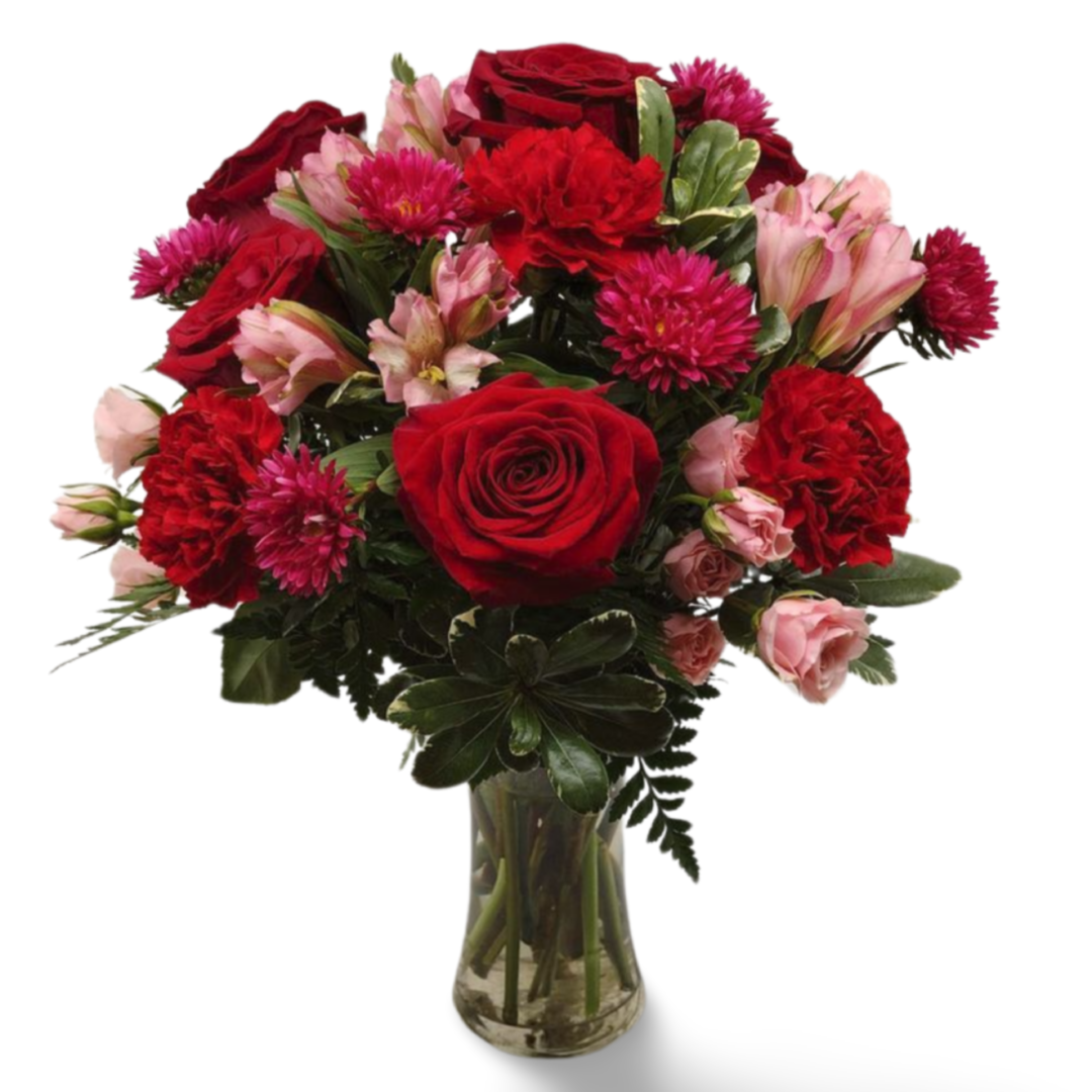 A bouquet of Ruby Radiance featuring red roses, pink carnations, and other blooms, arranged in a clear glass vase on a white background.